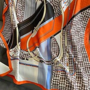 Close-up of silk scarf with orange and navy houndstooth pattern and equestrian bridle detail
