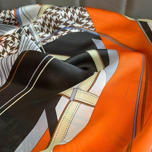 Detail of silk scarf showing orange and black houndstooth pattern with equestrian motifs