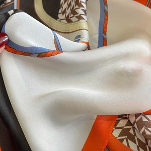 Close-up of houndstooth silk scarf with orange borders and glossy satin texture