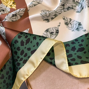 Detail of silk-like scarf featuring green leopard print and leafy pattern with yellow edges