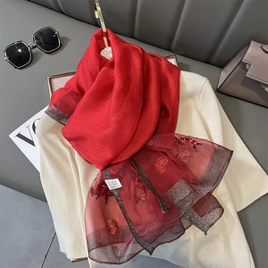 Detail of red silk blend scarf with delicate floral embroidery and sheer fabric textures