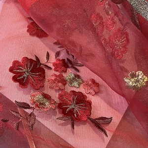 Detail showing intricate red floral embroidery with gold and silver threads on sheer silk scarf