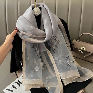 Detailed close-up of grey silk scarf with floral embroidery and metallic edges