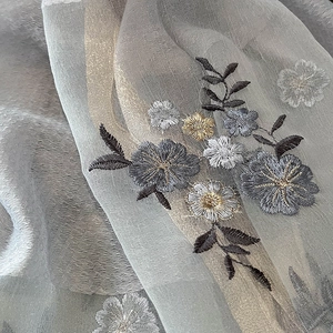 Macro detail of delicate floral embroidery on light grey semi-transparent silk blend fabric