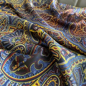 Détail d'un foulard en soie au motif paisley bleu et or montrant la texture satinée