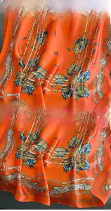 Detail of bright orange silk scarf featuring intricate feather and chain patterns