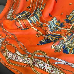 Detail of luxury orange silk scarf with gold chain and floral prints in satin finish