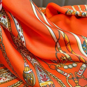 Macro detail of luxury orange silk scarf featuring vintage chain and buckle print patterns