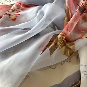 Detailed macro view of light gray scarf featuring elegant red floral print in soft silk