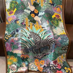 Zebra jungle print silk scarf with floral patterns displayed on a brown leather sofa