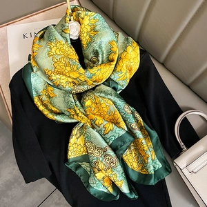 Elegant emerald silk scarf with yellow floral pattern draped on black sweater for styling