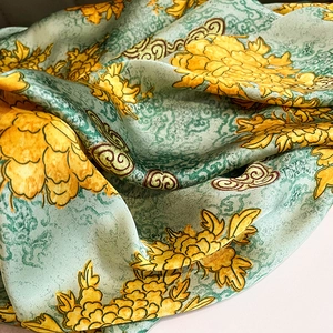 Detail of mint green silk scarf featuring yellow peony print and traditional cloud patterns