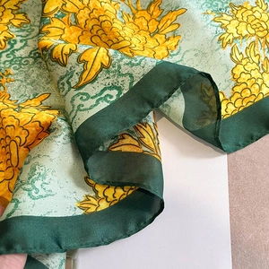 Detailed view of yellow peony print and green hem on soft silk feeling scarf fabric