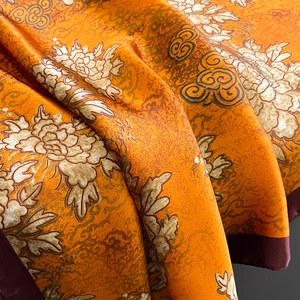 Detailed view of luxury silk scarf with orange peony floral pattern and smooth texture