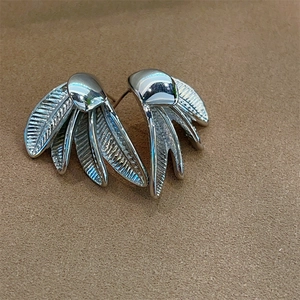 Chic silver feather wing stud earrings with textured finish on beige velvet background