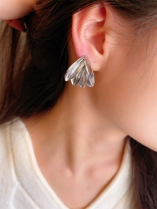 Close-up of silver-tone layered feather earrings with intricate texture on model