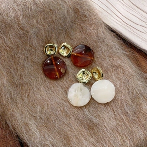 Détail de boucles d'oreilles en résine ambrée et crème avec attaches dorées carrées