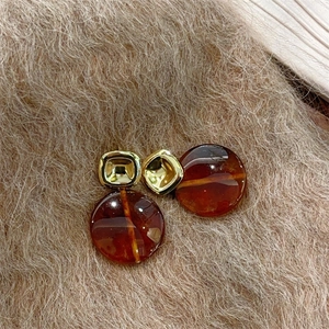 Détail de boucles d'oreilles rondes en résine ambre avec clous dorés sur fond en peluche