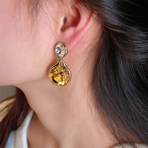Close-up of a model wearing faceted amber crystal drop earrings with gold settings