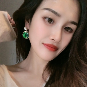 Close-up of elegant emerald green round drop earrings with crystal studs on female model