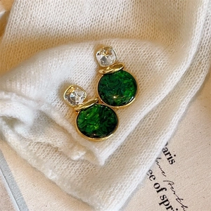 Detail of 925 silver needle gold earrings with green crystal on a white knit sweater