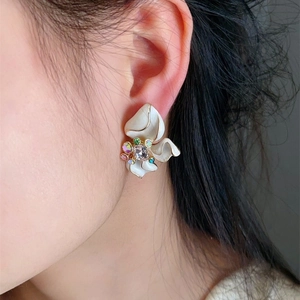 Detail of white enamel flower earring with gold edges and colorful rhinestones on model