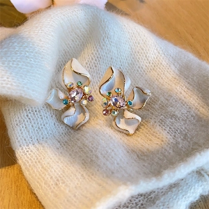 Macro shot of white enamel flower earrings with multicolored gemstones and gold trim