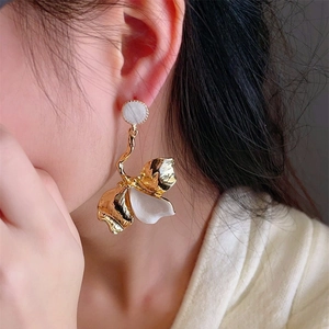 Close-up of oversized gold iris earrings with white enamel petals on a female model