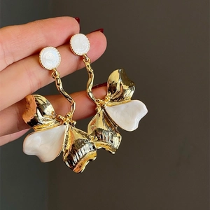 Detail of oversized gold metal floral earrings with white enamel petals and curved rods