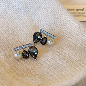 Unique seesaw earrings with black teardrop gems and white pearls on white knit fabric
