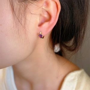 Golden heart earrings with purple crystals and sparkling zircons set on model's ear