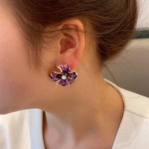 Detailed close-up of a purple enamel camellia earring with zircon inlays on a model