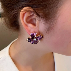 Close-up of purple enamel camellia stud earrings with gold edges and crystal center