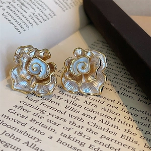 Macro detail of enamel camellia flower earrings with gold accents on a vintage book