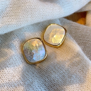 Macro shot of square gold earrings with white mother-of-pearl texture on knit fabric