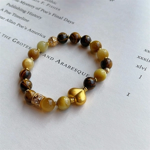 Vue macro des perles en œil de tigre et du pendentif cœur en or mat sur un bracelet