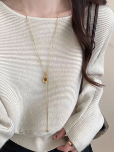 Detail of Y-shaped gold necklace with brown tiger eye stone on knit sweater
