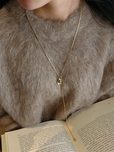 Close-up of a vintage golden Y-shaped tiger eye necklace on a brown sweater background