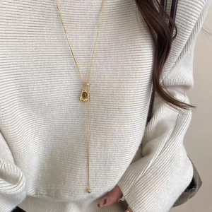 Elegant gold Y-shaped necklace with amber oval pendant worn over a beige sweater