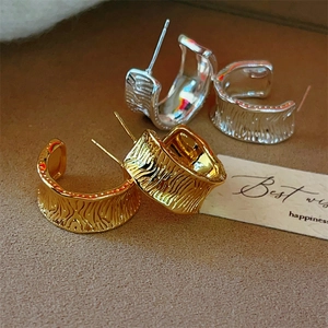 Macro shot of C-shaped hoop earrings with unique hammered texture in gold and silver
