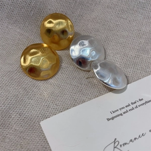 Detailed view of hammered gold and silver round stud earrings on linen texture background