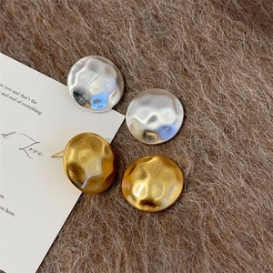 Macro detail of gold and silver disk earrings with a hammered textured finish on fur