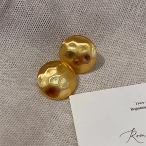 Detailed view of gold round textured earrings on a beige linen fabric background