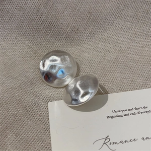 Macro shot of silver metal stud earrings with hand-hammered texture on linen