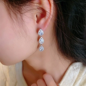 Macro detail of silver-tone triple pear-drop earrings with sparkling cubic zirconia inlay