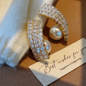 Detail of twisted gold earrings with pavé zircons and a large white pearl drop