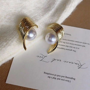 Macro detail of curved gold metal earring with vertical texture and embedded white pearl