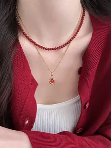 Close-up of double-layered necklace with red beads and gold gemstone pendant on a model