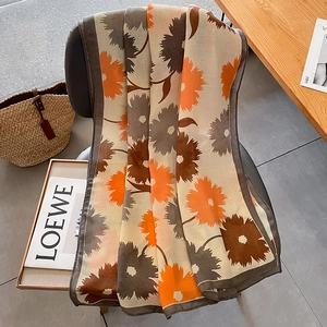 Écharpe artistique à imprimé floral beige et orange drapée élégamment sur une chaise