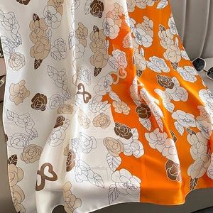 Détail d'un foulard en soie à motif camélia avec un design élégant orange et beige